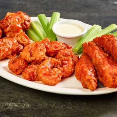 a plate of zingers, wings and shrimp tossed in buffalo sauce