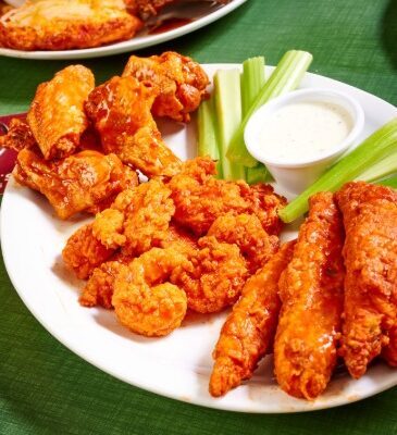 a plate of zingers, wings and shrimp tossed in buffalo sauce